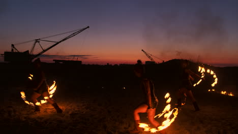 Professional-artists-show-a-fire-show-at-a-summer-festival-on-the-sand-in-slow-motion.-Fourth-person-acrobats-from-circus-work-with-fire-at-night-on-the-beach